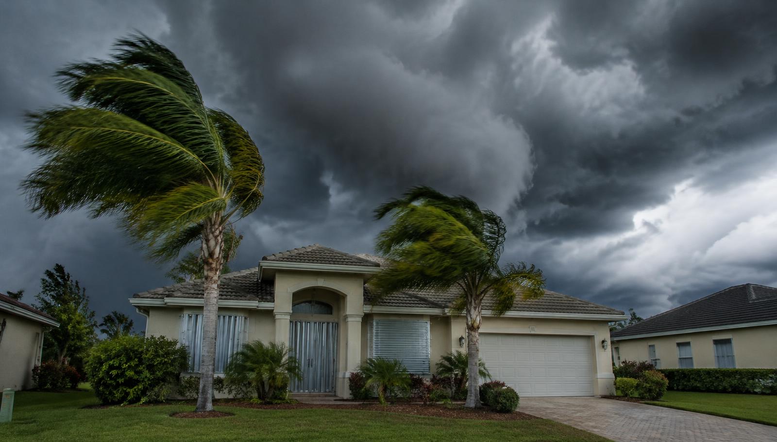 Central Florida home with storm shutters as hurricane clouds approach and palm trees bend